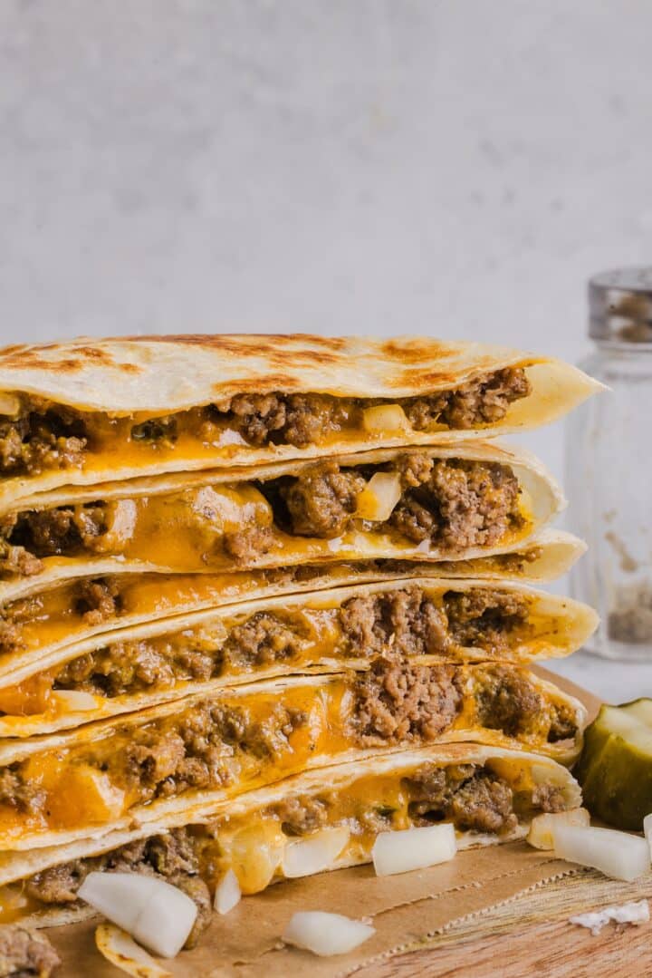 Cheeseburger quesadillas sliced and stacked on a wood cutting board.