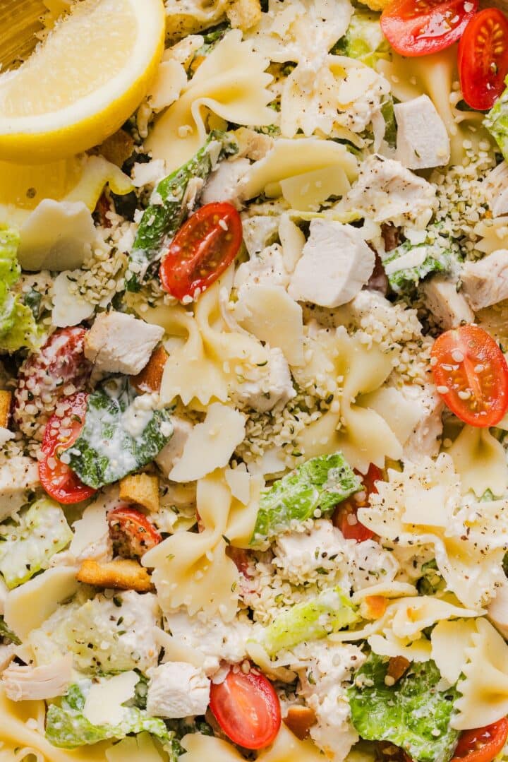 Chicken caesar pasta salad with farfalle pasta and halved cherry tomatoes.