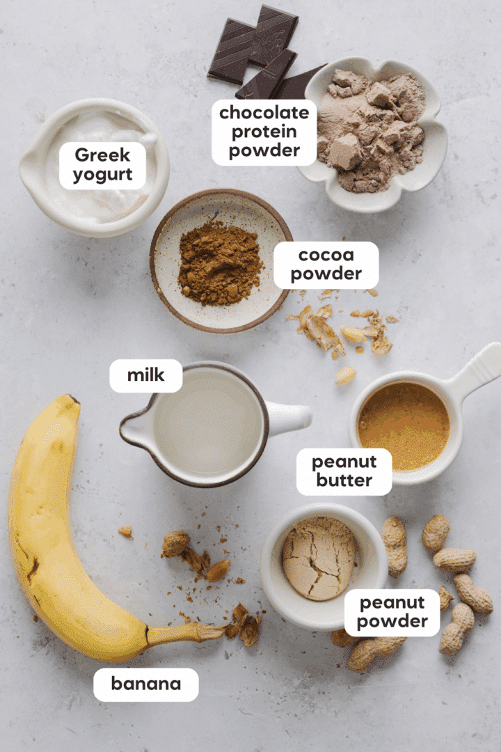 Ingredients for a chocolate peanut butter protein smoothie on a white marble counter.