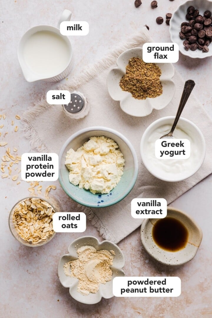 Ingredients for cookie dough overnight oats displayed in small bowls on a marble counter.