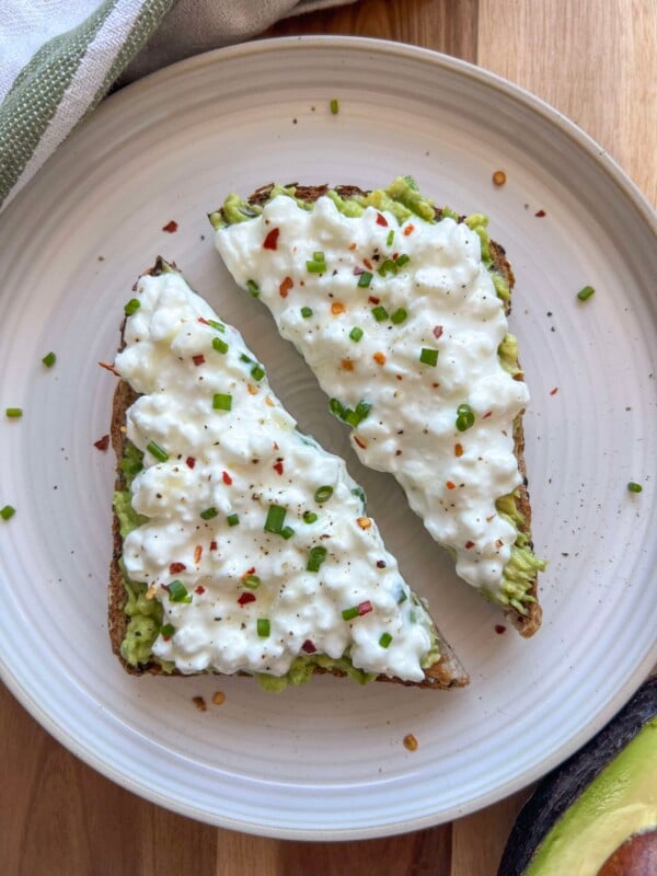 Cottage cheese avocado toast on a plate topped with chives, honey, and red pepper flakes