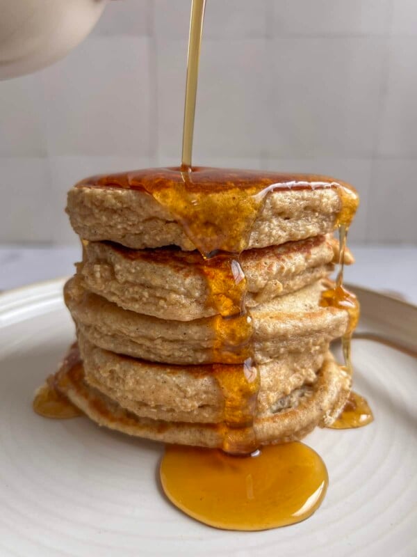 a stack of cottage cheese oatmeal pancakes on a plate with maple syrup being poured over them