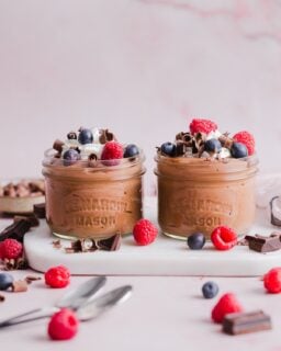 Two glass jars with cottage cheese chocolate mousse, topped with cream and berries.