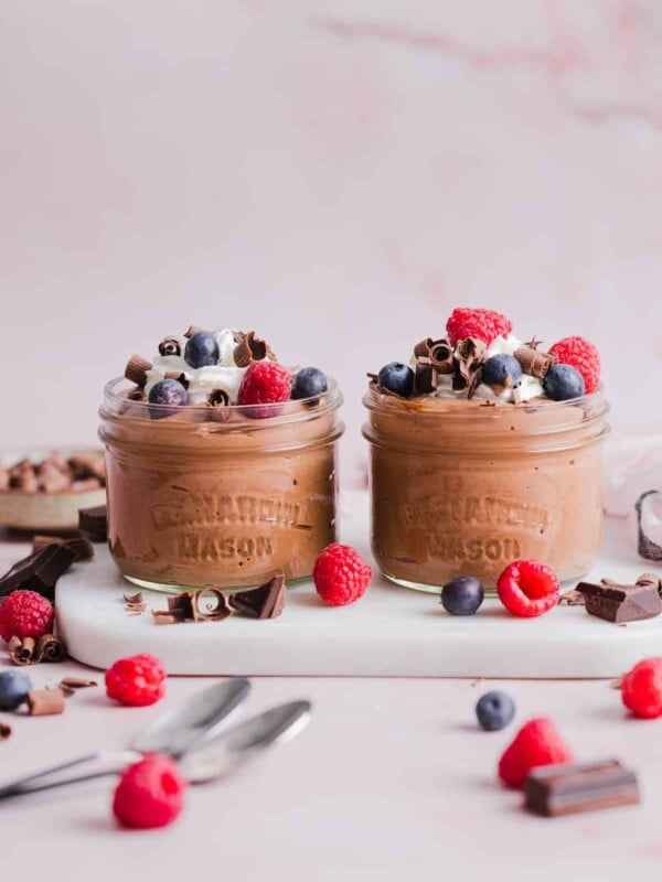 Two glass jars with cottage cheese chocolate mousse, topped with cream and berries.