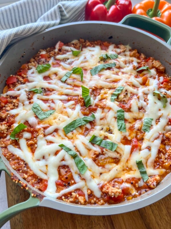 Large skillet with a quinoa stuffed pepper skillet, topped with shredded cheese and basil ribbons