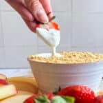 Woman's hand dipping a strawberry into cheesecake fruit dip topped with graham cracker crumbs