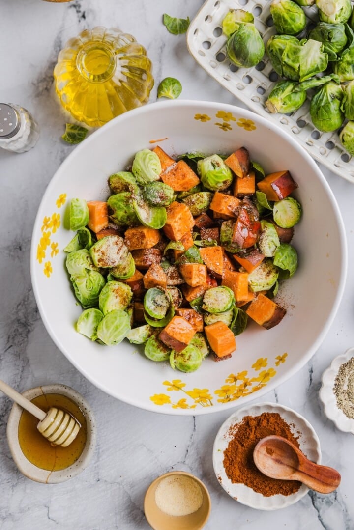 Brussels sprouts and sweet potatoes mixed in a bowl with seasoning.