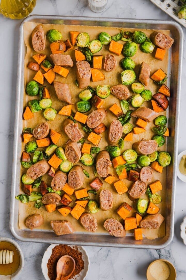 Vegetables on a parchment-lined sheet pan with sliced chicken sausage.