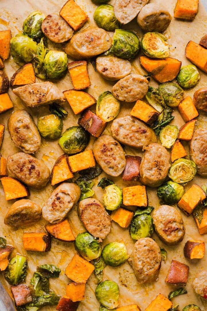 Roasted vegetables and chicken sausage coins on a sheet pan.