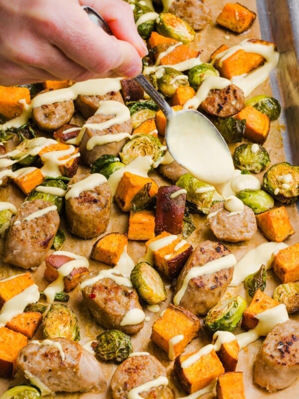 Chicken sausage sheet pan dinner with yogurt honey mustard being drizzled over top.