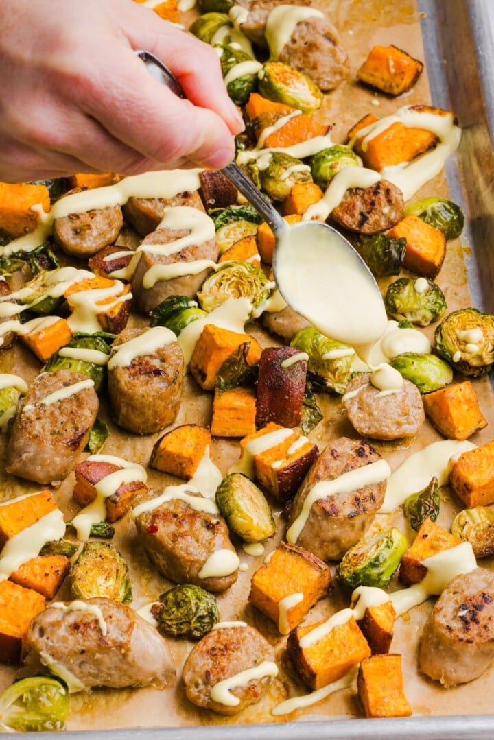 Chicken sausage sheet pan dinner with yogurt honey mustard being drizzled over top.