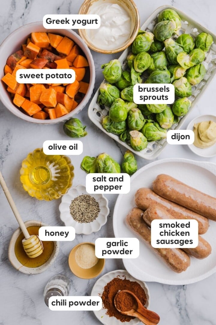 Ingredients for chicken sausage sheet pan dinner in bowls on a marble counter top.