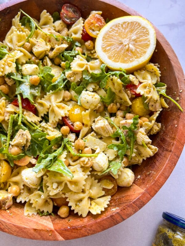 Chicken pesto pasta salad tossed in a large wooden serving bowl, served with half a lemon