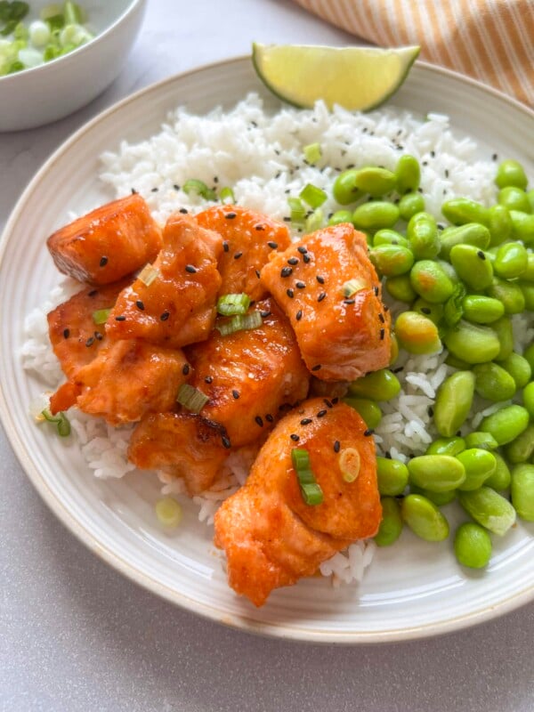 Small white plate with rice, edamame, and hot honey salmon bites.