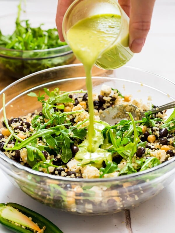 Quinoa and arugula salad with honey jalapeno green dressing being poured over