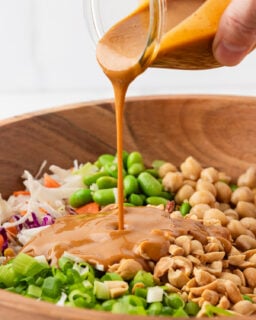 Creamy peanut dressing being poured over quinoa edamame salad.