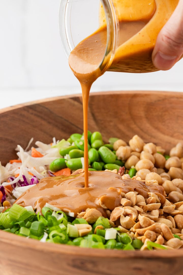 Creamy peanut dressing being poured over quinoa edamame salad.