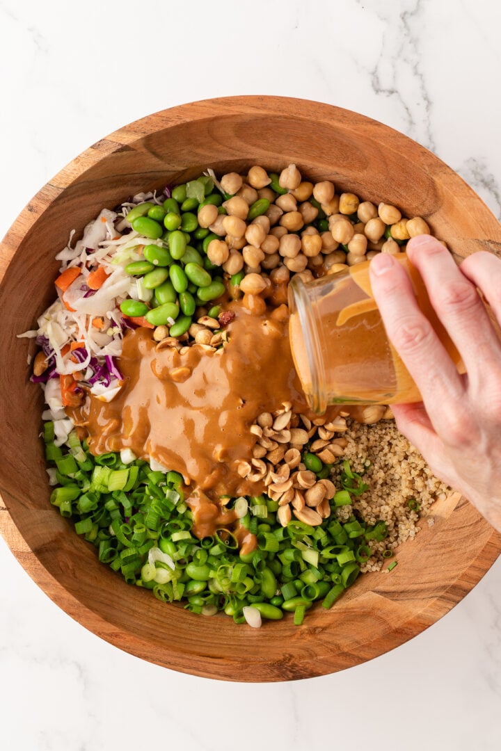 Quinoa edamame salad in a large wooden bowl with dressing poured over top.