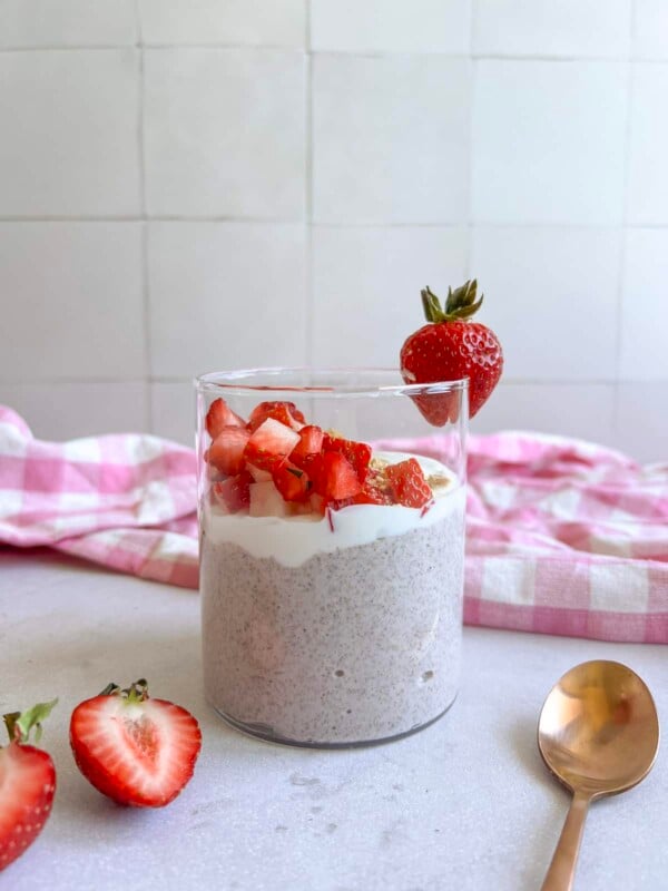Glass jar containing blended strawberry cheesecake chia pudding, topped with yogurt, strawberries, and graham cracker crumbs