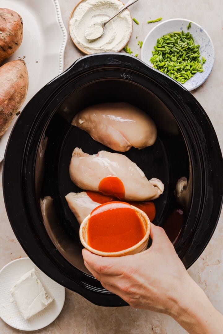 Raw chicken breast and buffalo sauce in slow cooker for buffalo chicken sweet potatoes.