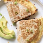 Two halves of a breakfast quesadilla with egg and cheese on a plate with avocado slices