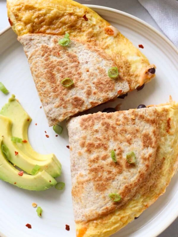 Two halves of a breakfast quesadilla with egg and cheese on a plate with avocado slices