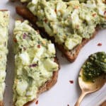 White plate with 2 slices of toast topped with pesto egg salad
