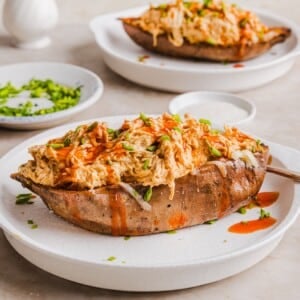 Buffalo chicken sweet potato boats in the slow cooker, topped with shredded cheese and chives.