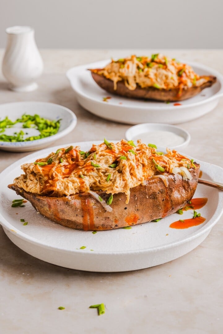 Buffalo chicken sweet potato boats in the slow cooker, topped with shredded cheese and chives.