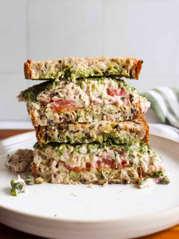 Tunacado sandwich on seedy whole wheat bread, sliced in half on a white plate