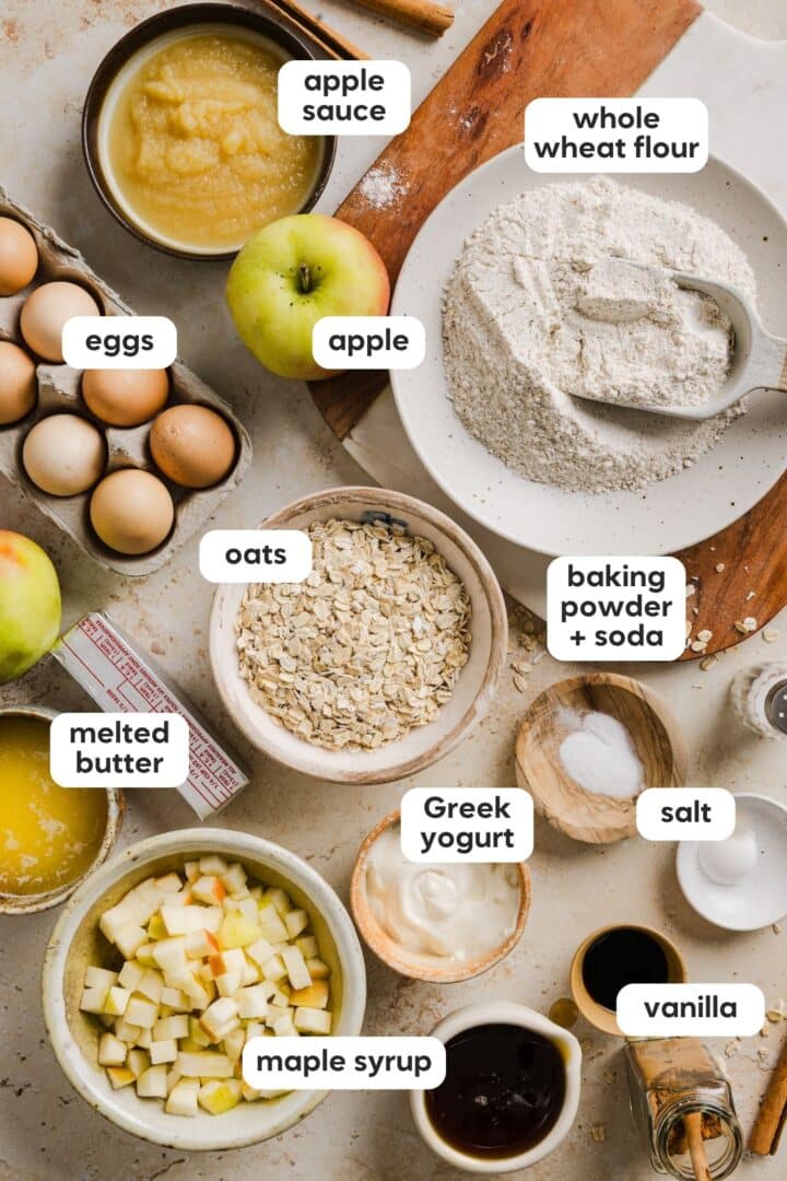 Ingredients for apple cinnamon oat muffins displayed in small bowls on a marble counter top.