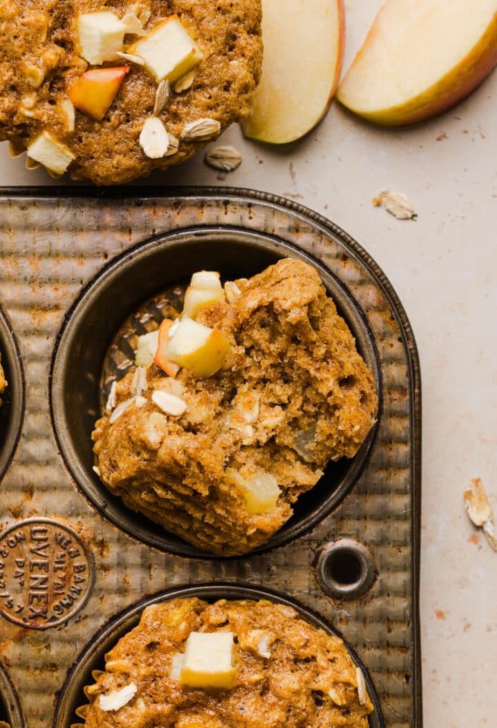Apple cinnamon oatmeal muffins in a pan, with a bite taken out.