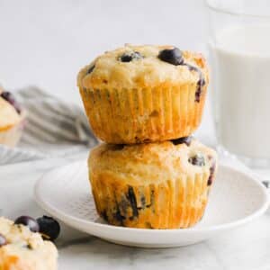 Two high-protein blueberry muffins stacked on a white plate.