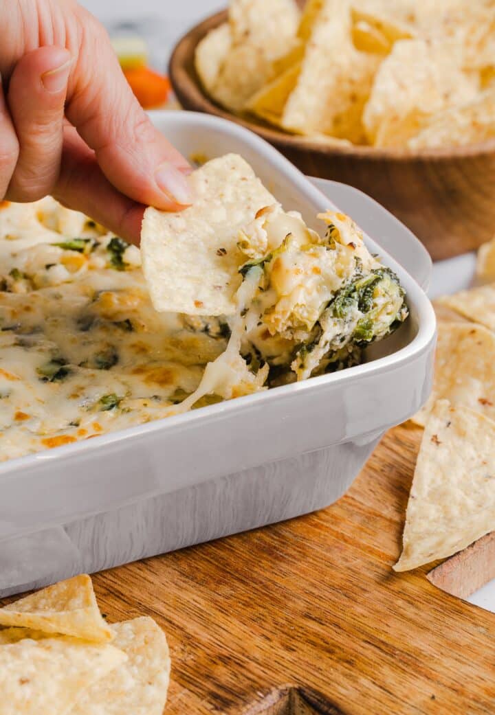 Healthy spinach artichoke dip without mayo or sour cream being scooped with a tortilla chip.