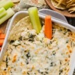 Healthy spinach artichoke dip in a grey baking dish with tortilla chips.