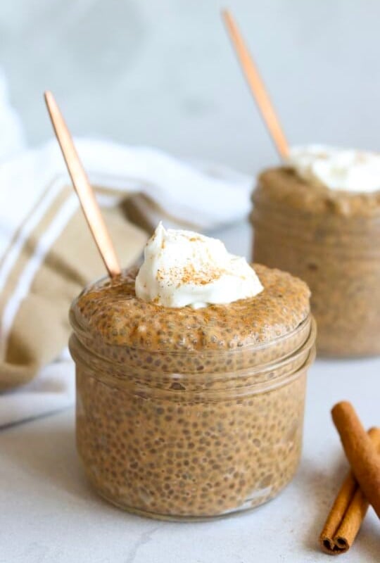 Two glass jars filled with pumpkin chia seed pudding topped with yogurt and cinnamon