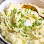 White serving bowl with boursin cheese mashed potatoes with chives and a gold serving spoon