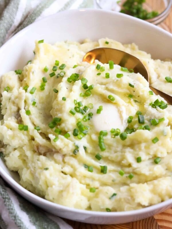 White serving bowl with boursin cheese mashed potatoes with chives and a gold serving spoon