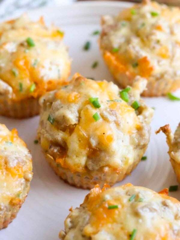 Several sausage cheese muffins arranged on a white plate, topped with sliced chives