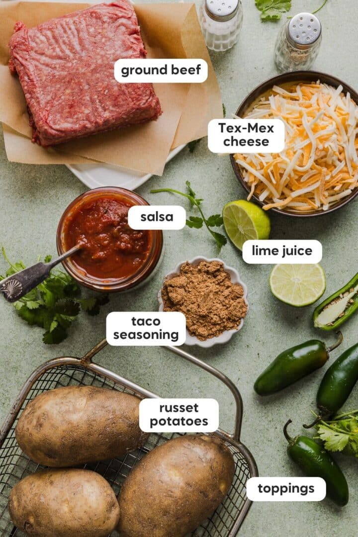 Ingredients for taco baked potatoes displayed in small bowls on a green marble counter.