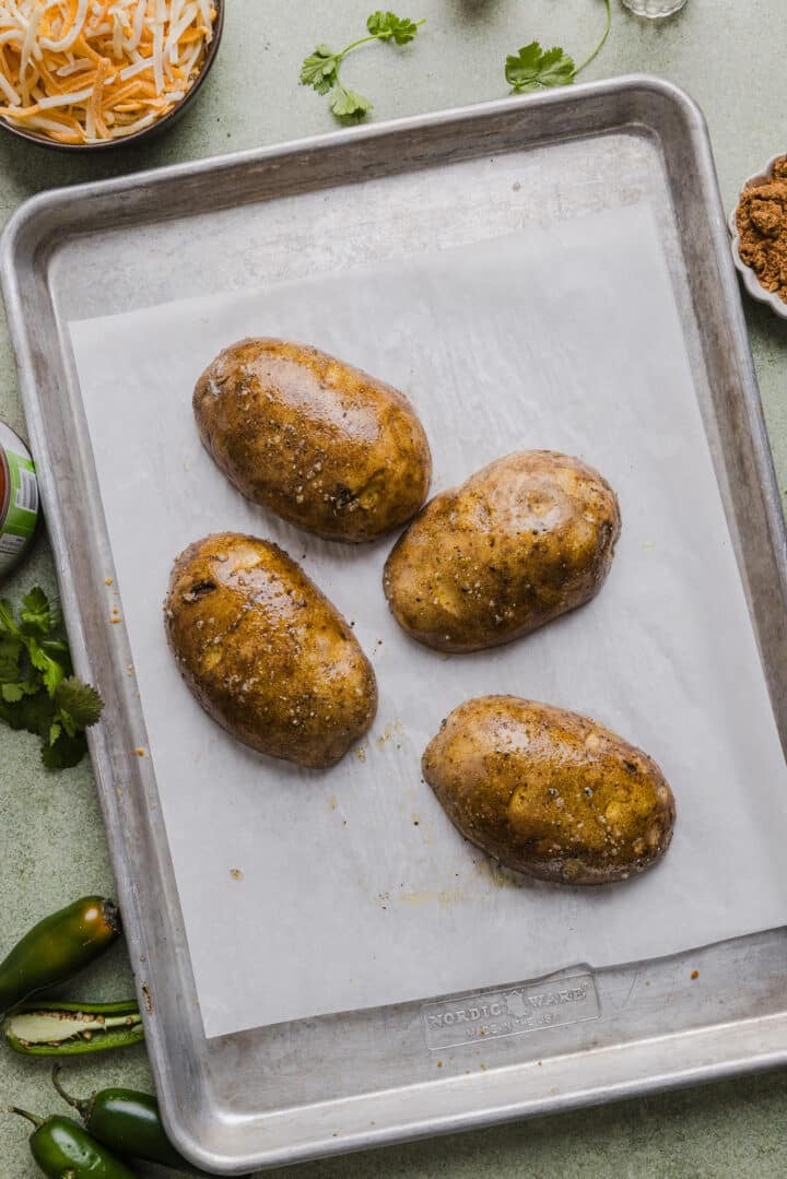 Seasoned baked potatoes sliced in half and placed on a parchment-lined sheet pan.