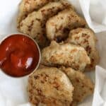 A white bowl with parchment paper containing several chicken sausage patties with a small ketchup bowl