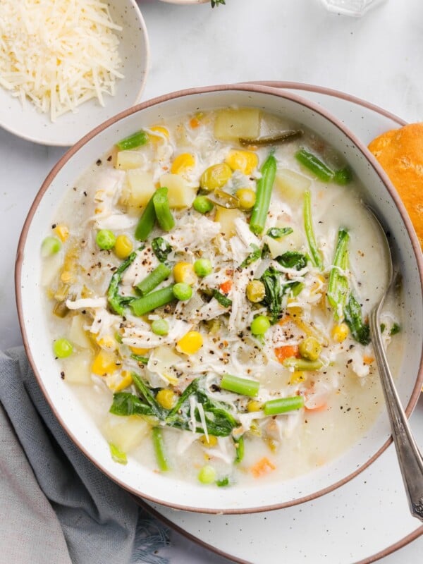 Chicken pot pie soup in a shallow white bowl, served with a biscuit