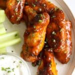 Honey buffalo wings garnished with chives on a plate with celery sticks and ranch