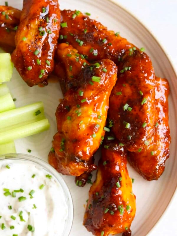 Honey buffalo wings garnished with chives on a plate with celery sticks and ranch