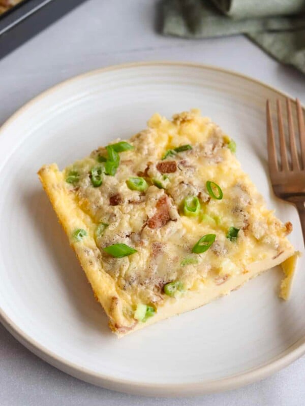 Slice of cottage cheese egg bake on a white plate, garnished with sliced green onions