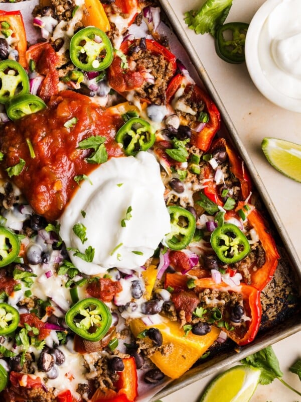 Healthy bell pepper nachos topped with a big dollop of greek yogurt and salsa, on a sheet tray
