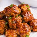 A pile of juicy BBQ chicken meatballs stacked on a white plate, garnished with diced chives