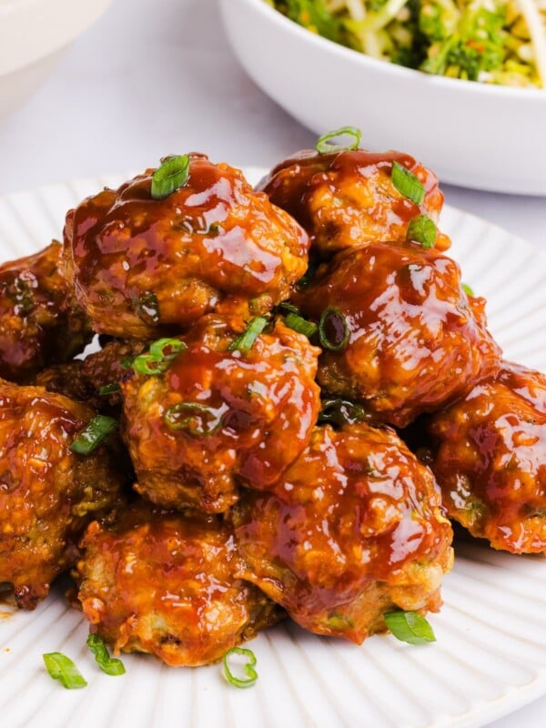 A pile of juicy BBQ chicken meatballs stacked on a white plate, garnished with diced chives