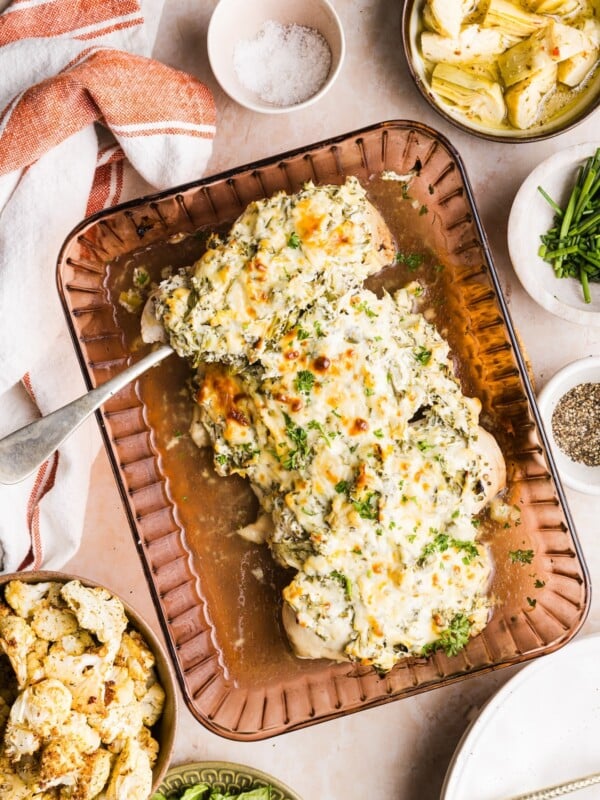 Glass baking tray filled with spinach artichoke chicken bake, displayed on a warm-toned marble counter